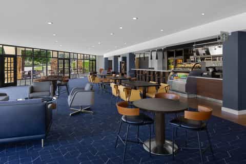 Modern hotel lobby and café with blue seating, wooden tables, coffee counter, and large windows