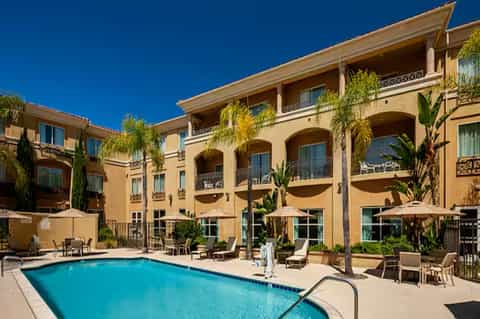 Mediterranean-style resort building with arched windows, balconies, and swimming pool surrounded by lounge chairs