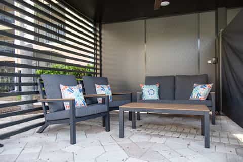 Modern patio lounge with dark outdoor furniture, colorful throw pillows, horizontal black slat privacy screen, and stone flooring
