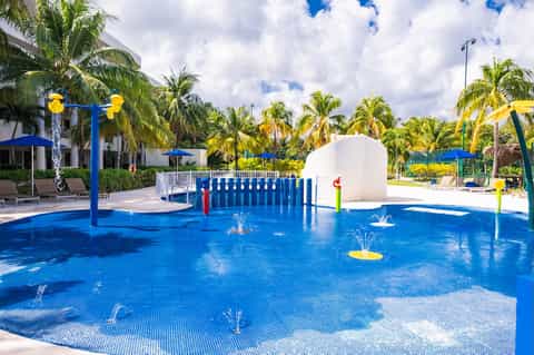 Colorful splash pad with blue water features, yellow columns, and tropical vegetation