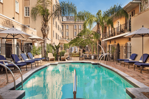 Courtyard pool surrounded by historic buildings with palm trees and lounge chairs