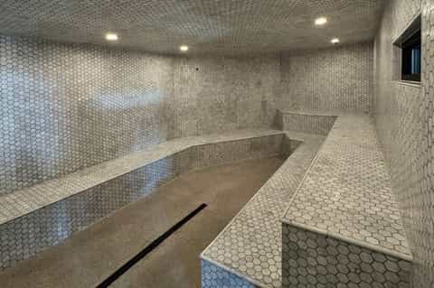 Contemporary steam room with hexagonal tile walls, wooden bench seating, and recessed lighting