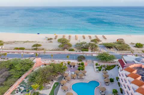 Aerial view of turquoise pool, beach access, palm trees, and pink pathway connecting beachfront resort to ocean