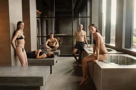 Modern indoor spa area with soaking tub and five people in swimwear on stepping platforms