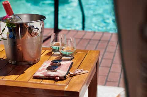 Poolside wine service with ice bucket, glasses, and charcuterie on wooden table