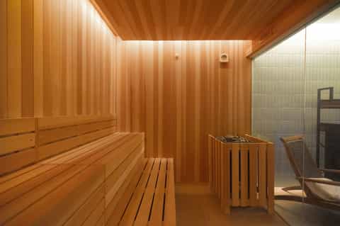Wooden sauna interior with benches, traditional heater basket, and glass shower enclosure