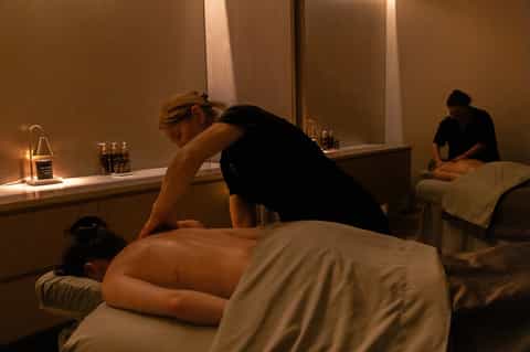 Spa massage treatment room with therapist performing massage on client in warm, ambient lighting