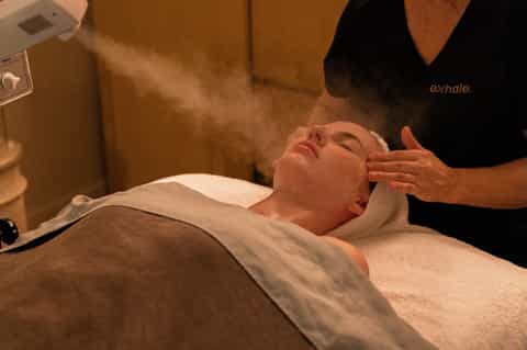 Spa treatment room showing therapist performing facial massage on relaxed client at wellness center