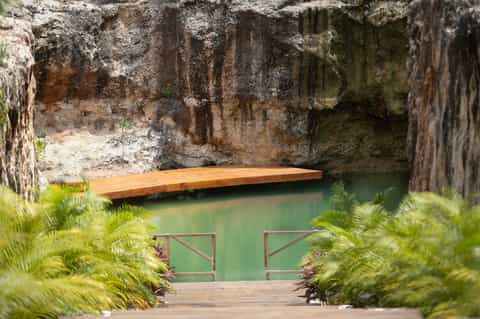 Natural stone courtyard with wooden deck bridge over turquoise water and lush greenery