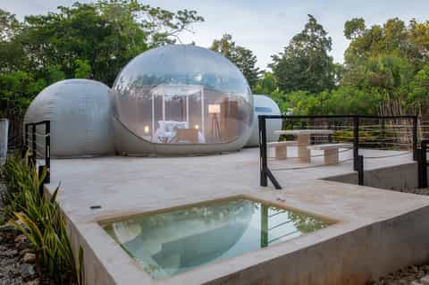 Futuristic bubble pod accommodation with small pool surrounded by desert vegetation