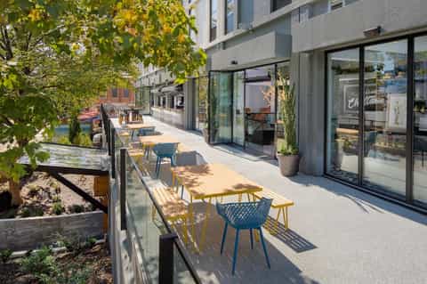 Outdoor terrace with modern seating, green plants, and glass storefront overlooking waterfront