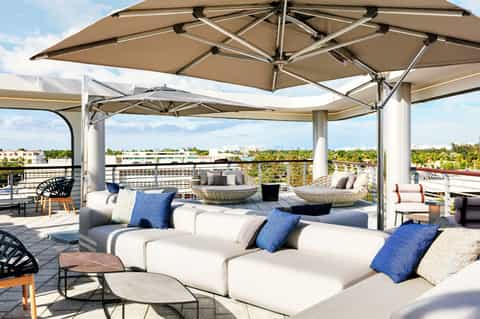 Rooftop lounge with modern white seating, tan umbrellas, and city skyline views