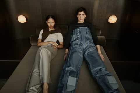 Two people sitting on modern gray bench in minimalist room with round wall lights