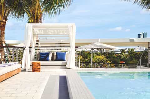 Luxury poolside cabana with white curtains, palm trees, and ocean view from elevated terrace