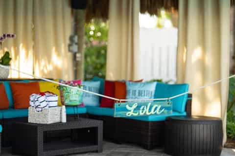 Colorful outdoor lounge with turquoise and orange cushioned seating, cream curtains, and patio string lights