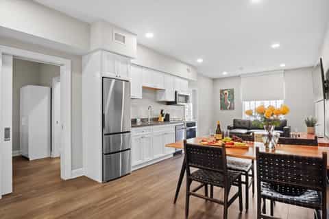 Bright modern apartment kitchen with white cabinetry, stainless steel appliances, and dining table