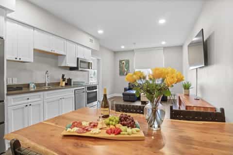 Bright kitchen and dining area with white cabinetry, wood table, and yellow flowers