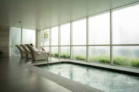Serene indoor spa pool with lounge chairs overlooking tranquil landscaped grounds through floor-to-ceiling windows