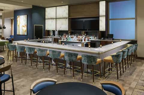 Upscale hotel bar lounge with marble-top counter, teal bar stools, and sophisticated ambiance