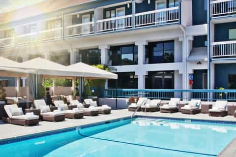 Resort pool with lounge chairs, white umbrellas, and modern multi-story building with balconies