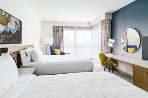 Contemporary hotel room with twin beds, blue accent wall, patterned curtains, and sea-view balcony
