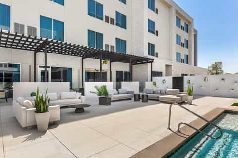 Modern resort terrace with white lounge furniture, pergola, and infinity pool with city view