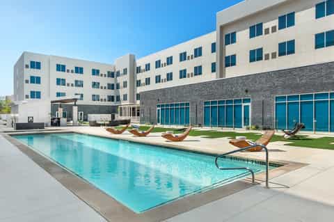 Modern resort building with lap pool, lounge chairs, and contemporary architecture under clear sky