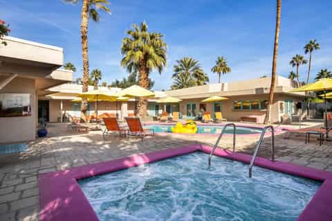 Resort courtyard with purple hot tub, yellow umbrellas, palm trees, and colorful loungers