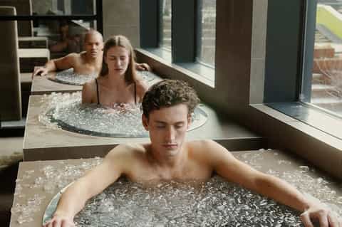Guests relaxing in natural hot spring pools with large windows overlooking scenic landscape