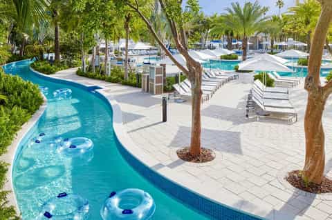 Lazy river with inflatable tubes winding through palm-lined resort deck with lounge chairs