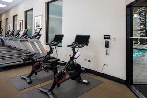 Fitness center with spinning bikes, treadmills, and large windows overlooking pool area