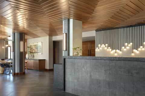Contemporary hotel lobby with wooden slat ceiling, concrete desk, pendant lighting, and modern design