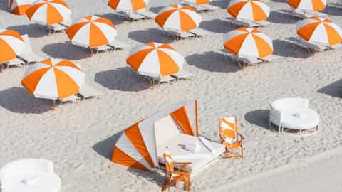 Beach amenities with rows of orange and white umbrellas and striped beach tents on sandy shore