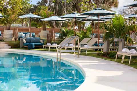 Resort pool with umbrellas, lounge chairs, tropical landscaping, and blue water