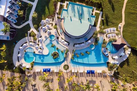 Aerial view of resort with curved pools, landscaping, and beachfront lounge areas