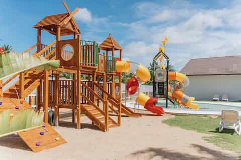 Colorful wooden playground with slides, climbing structures, and water slide on sandy beach area