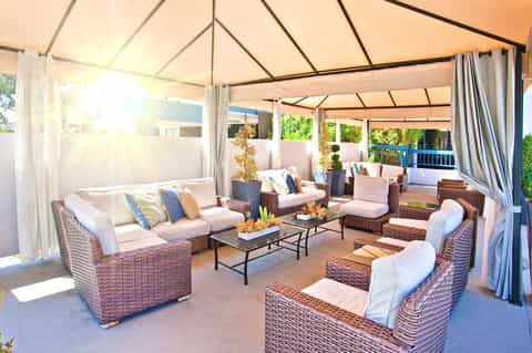 Covered outdoor lounge area with wicker furniture, cream cushions, and flowing white curtains in a luxury resort setting