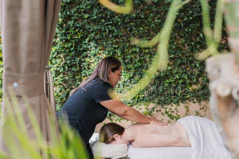 Outdoor spa massage treatment under ivy-covered pergola with natural green plant backdrop