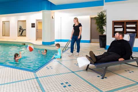 Indoor family pool area with children playing, staff supervising, and lounge seating