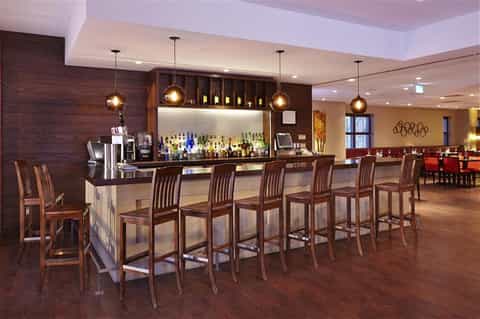 Upscale hotel bar with dark wood paneling, pendant lighting, stocked shelves, and bar seating