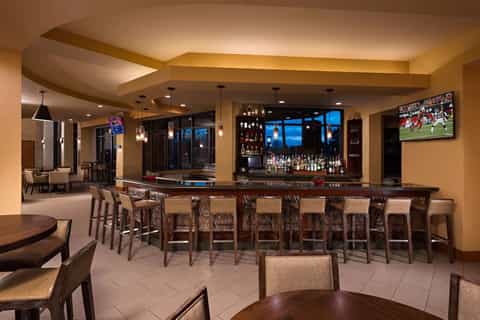 Upscale hotel bar and lounge with long counter, seating, pendant lighting, and evening views