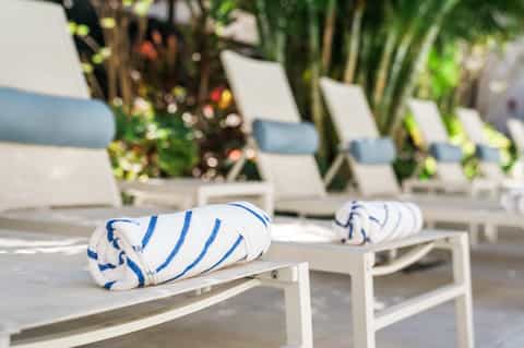 Close-up of striped blue and white towels on lounge chair by pool with greenery background