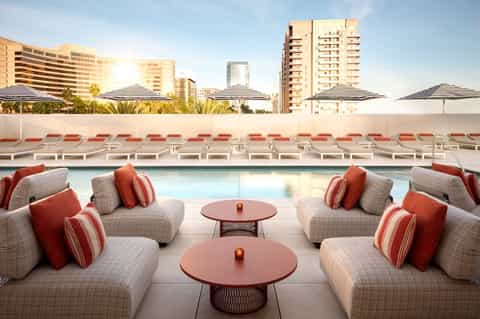 Resort pool deck with red and white lounge seating, umbrellas, and city skyline view