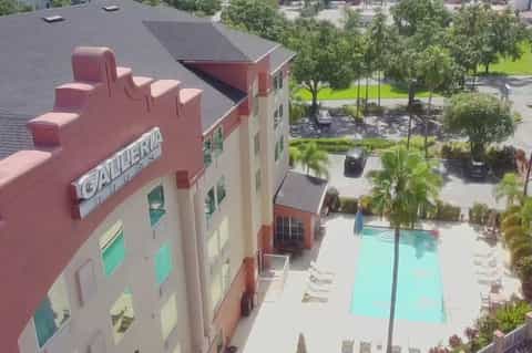 Aerial view of residential complex with colorful building, pool, green landscaping, and surrounding development