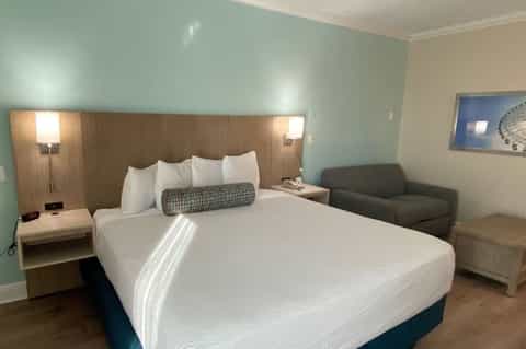 Modern hotel room with queen bed, mint green accent wall, wood headboard with reading lights, and armchair.