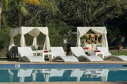 Poolside cabanas with white curtains, lounge chairs, and spa treatment beds near swimming pool