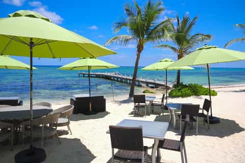 Beach resort area with lime-green umbrellas, palm trees, wooden pier, and turquoise ocean