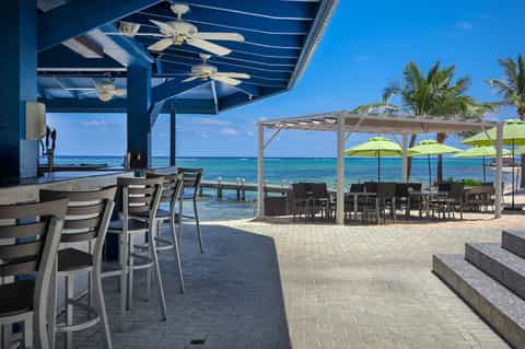 Beachfront bar and dining area with blue pergola, turquoise umbrellas, and ocean view