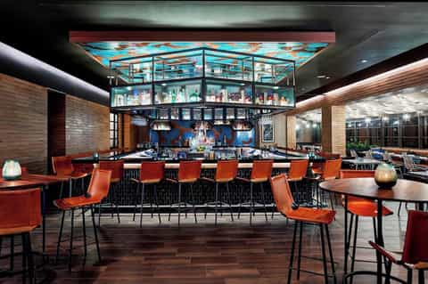 Modern hotel bar lounge with red leather seating, turquoise ceiling art, and multiple levels