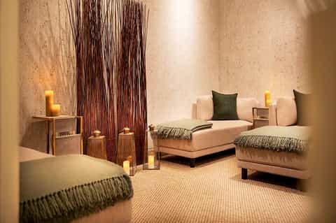 Luxury spa lounge with cream-colored seating, dark woven wall installation, candles, and earthy tones